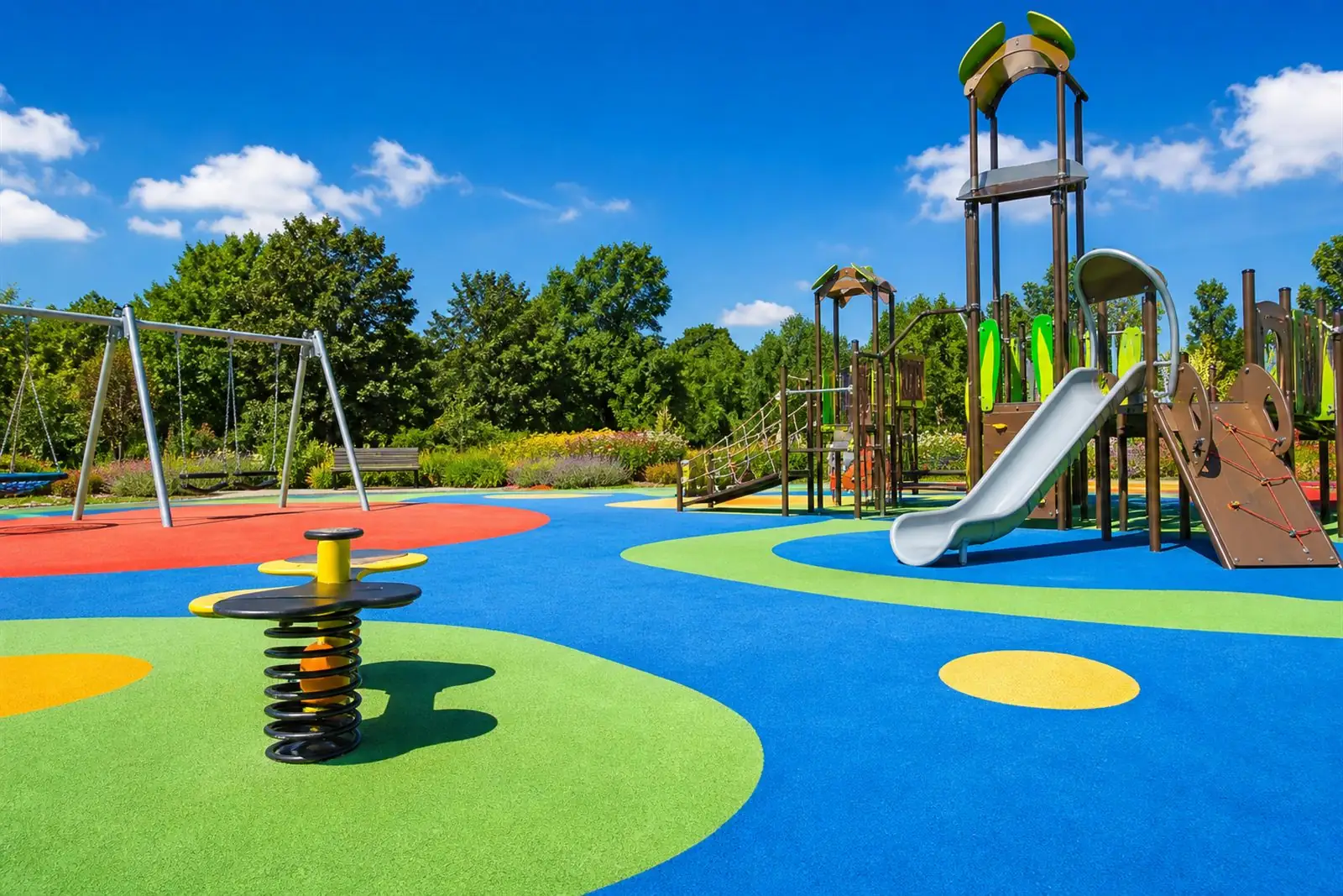 Modern British playground with colourful wetpour rubber safety surfacing, a slide and swings on a sunny day
